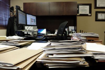 Overloaded office desk with stacked files and folders representing burdened employees during executive search