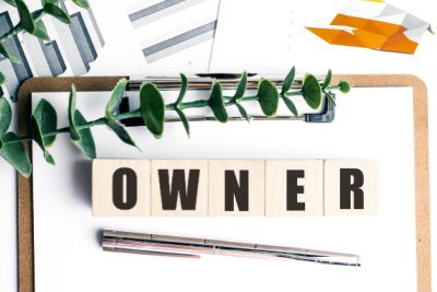 Wooden blocks spelling owner on clipboard with financial charts, representing executive search for owner operated businesses in Michigan